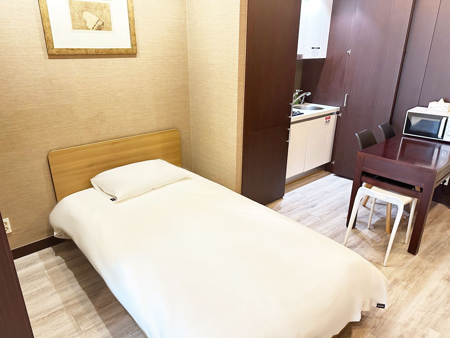 Habitación de hotel con una cama individual, un escritorio pequeño con una silla, un microondas y un lavamanos.