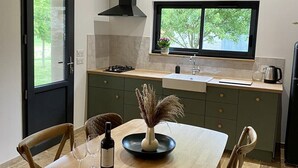 A modern kitchen with a dining area, featuring a large window, a built-in stove, and a black range hood. - Charming 80m2 house in the countryside (Montpezat)