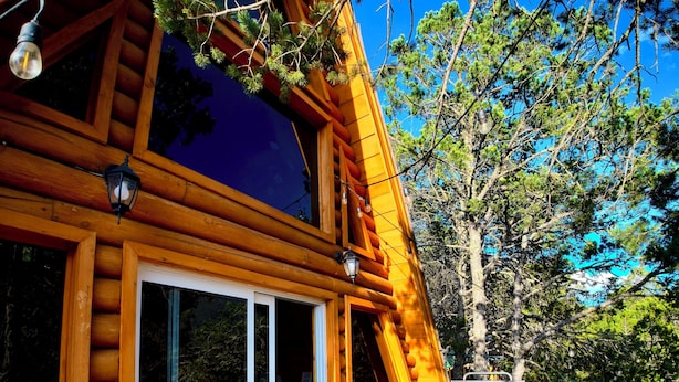 A wooden cabin with a deck, large windows, and a grill.