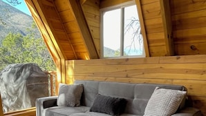 A grey sofa with a matching ottoman in a wooden cabin with a large window.