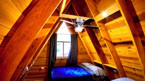 A room with wooden beams, a sloped ceiling, a ceiling fan, and two beds with blue bedding.