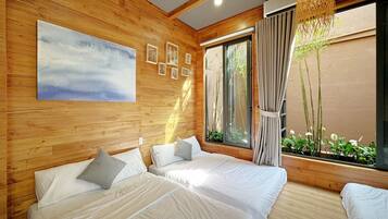 A room with wooden walls, two beds with white linens, a large window with a view of greenery, and a hanging light fixture.