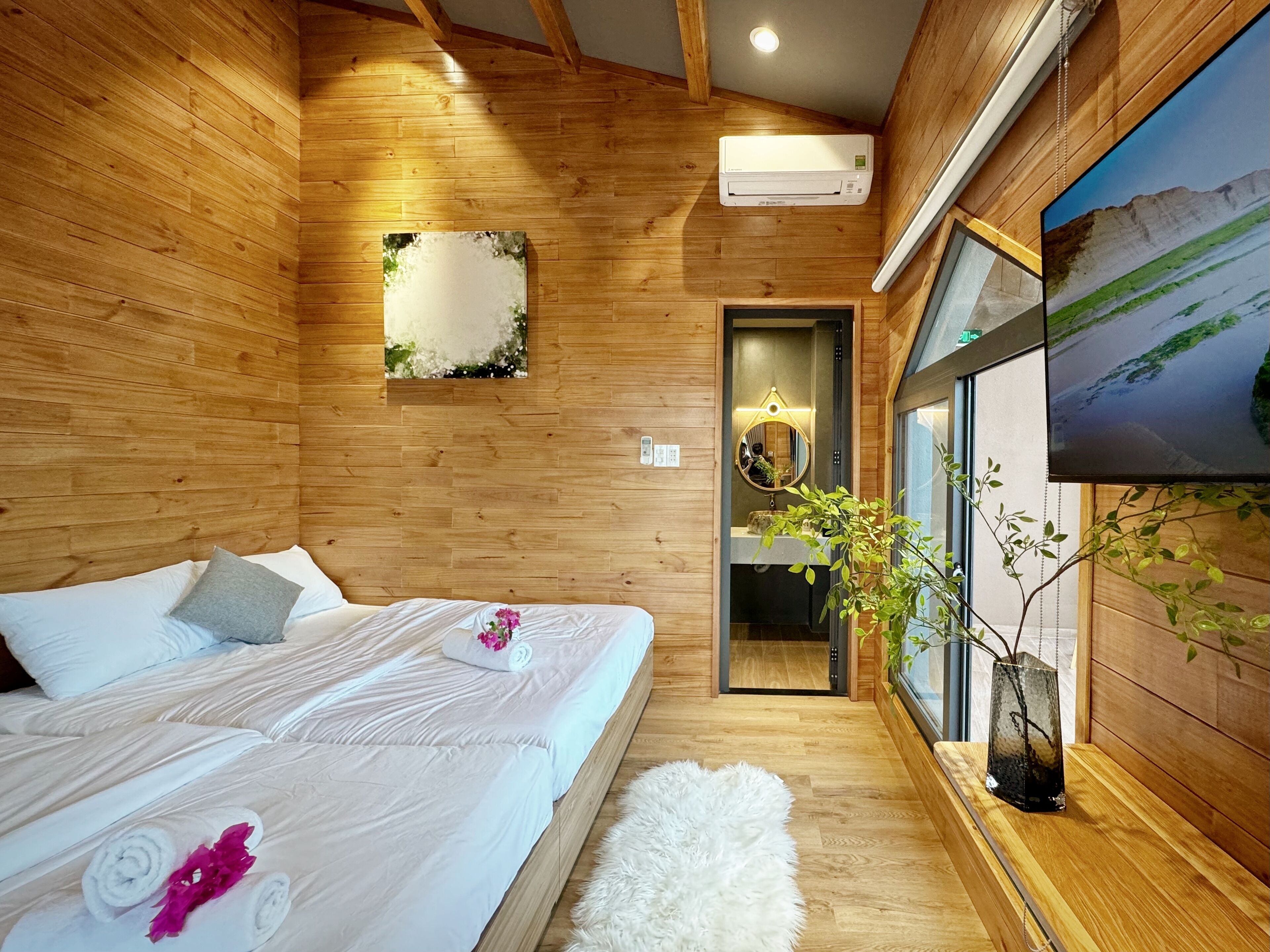 A wooden-paneled bedroom with a bed, a mirror, a wall-mounted air conditioner, and a window with a view.