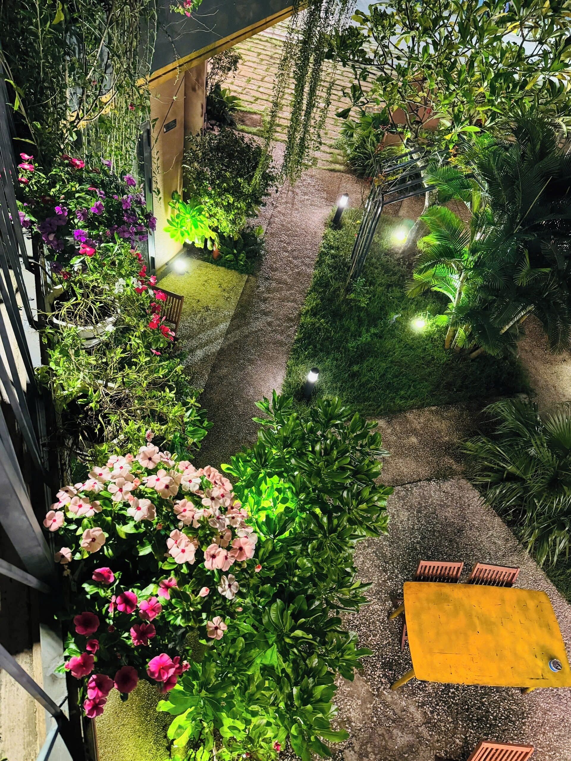 Um jardim com diversas plantas e flores, um caminho de cascalho e uma mesa amarela.