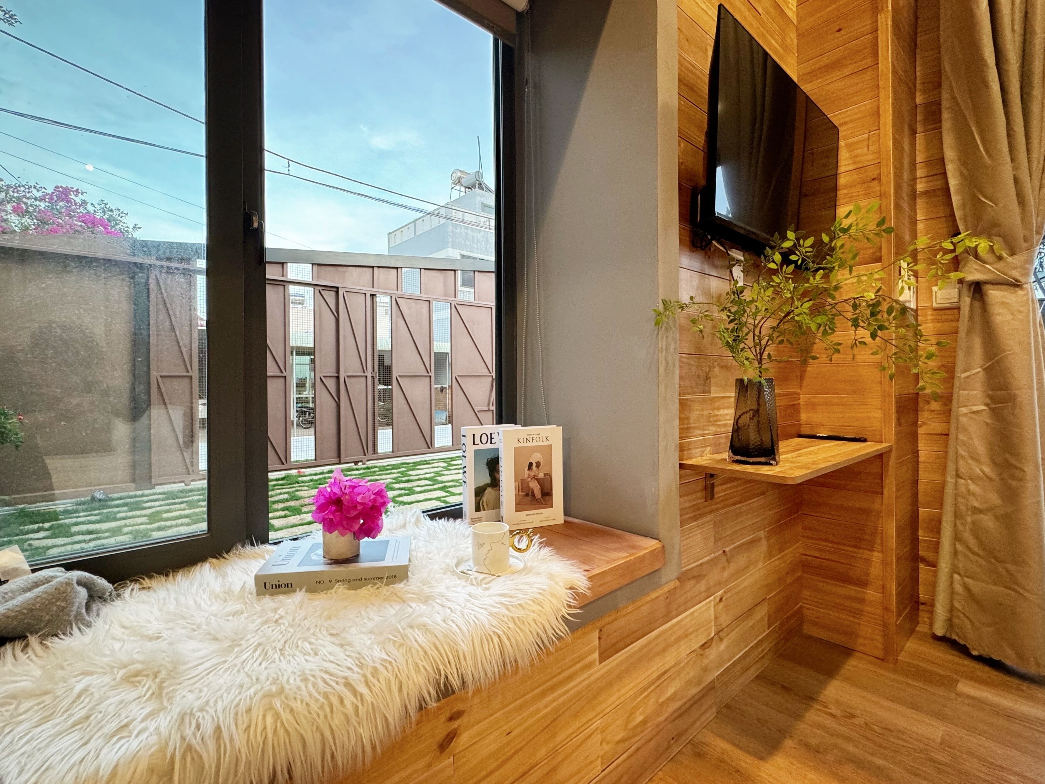 A modern room with a large window, wooden wall paneling, a mounted TV, and a small shelf with a plant.