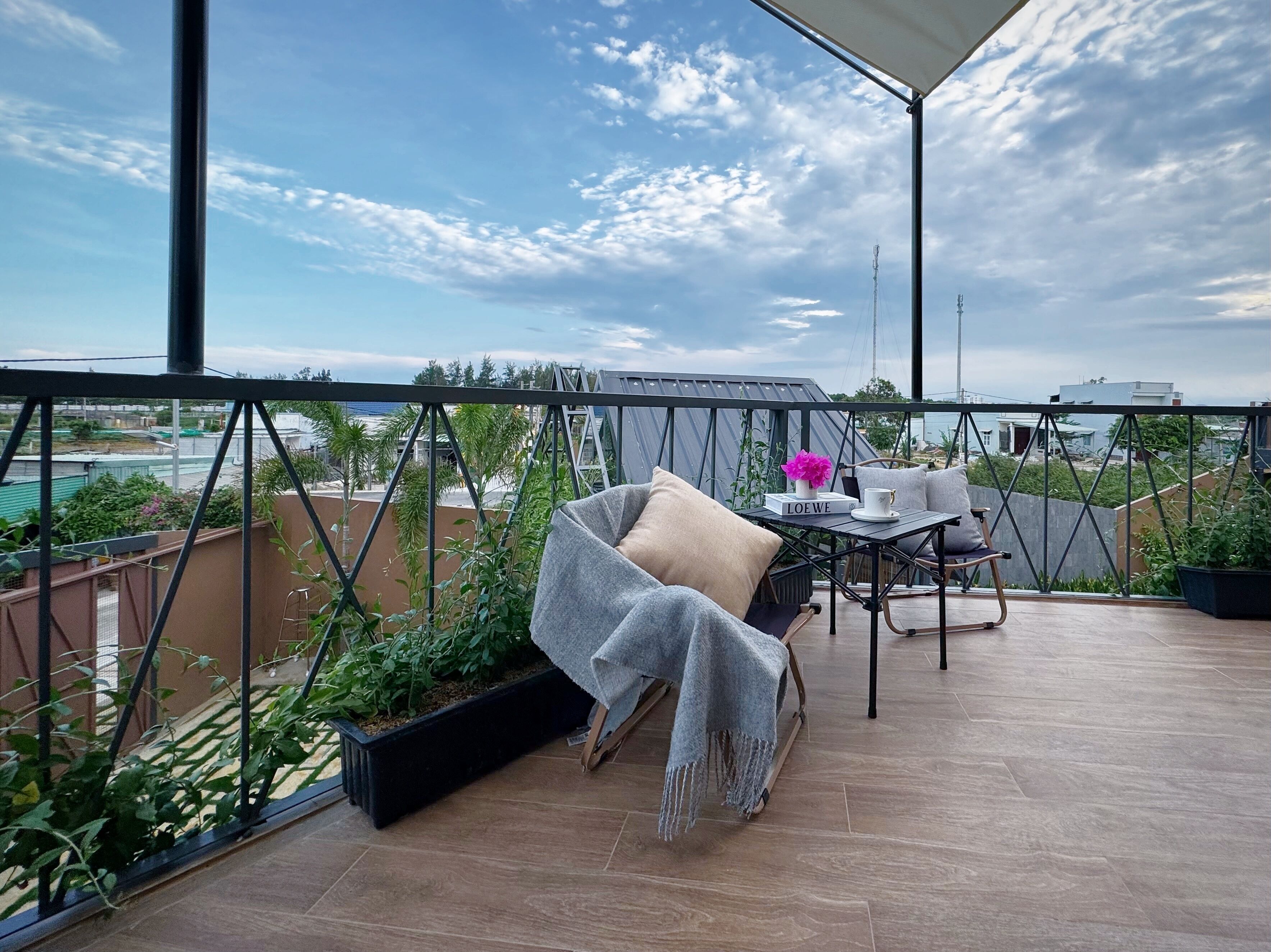 A balcony with a view of the city, a table with a book and a cup, and a chair with a blanket.