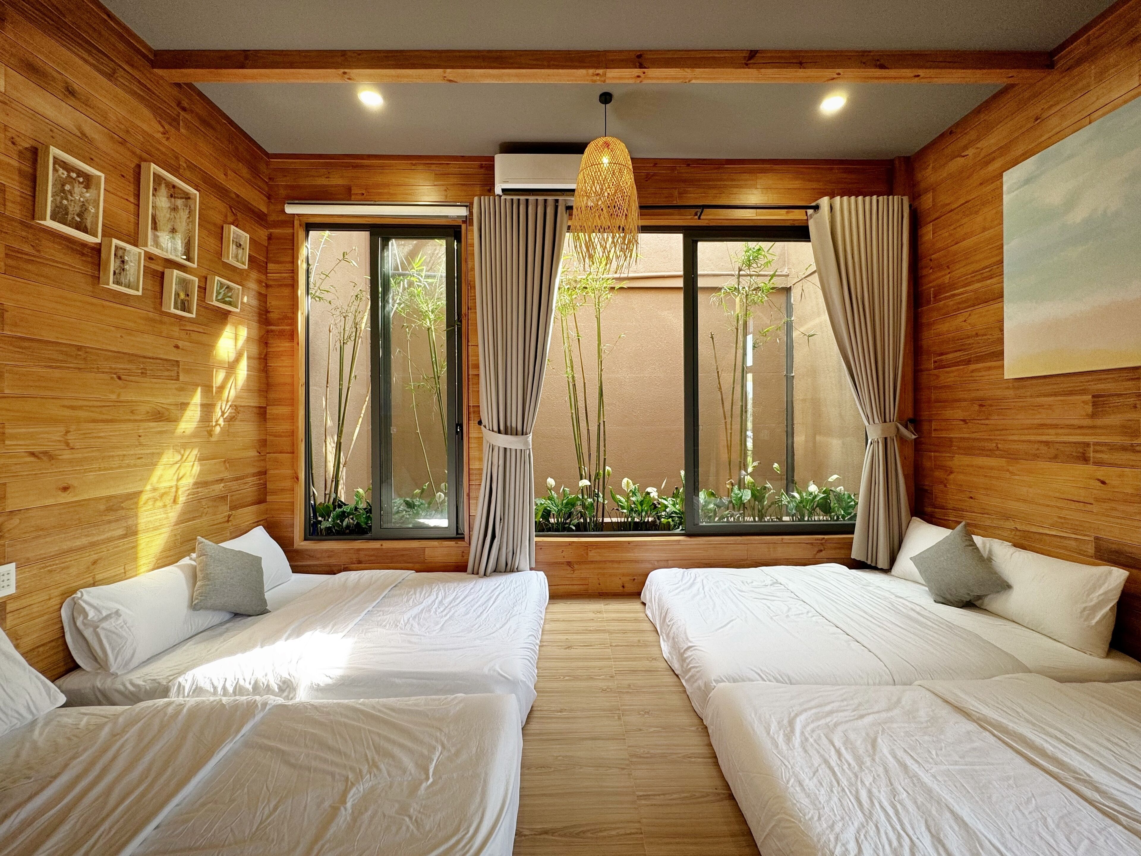 A room with wooden walls, two beds, a large window with curtains, and a hanging light fixture.