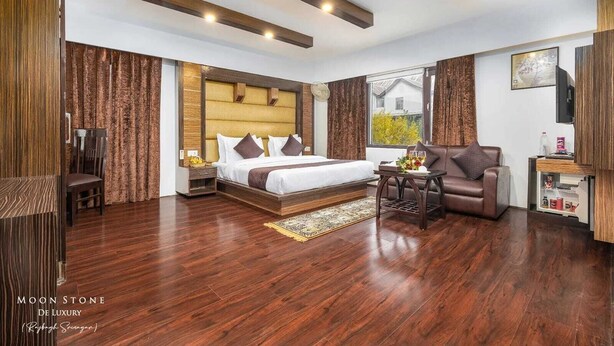 A modern hotel room with a large bed, a sofa, a small table, and a TV. - Hotel Moonstone de luxury (Srinagar)