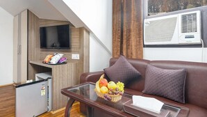 A compact living space with a sofa, a glass coffee table with fruit, a TV, a mini-fridge, and a window with a view. - Hotel Moonstone de luxury (Srinagar)