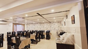 A dining area with multiple tables and chairs, a kitchen counter, and a patterned wall. - Hotel Moonstone de luxury (Srinagar)