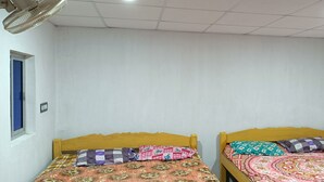 Two single beds with wooden headboards, white walls, a ceiling fan, and a window with a blue frame. - Bagda Beach Resort (Balasore)