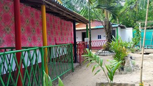 A building with a patterned exterior wall, a green and red metal fence, and a small garden area with plants. - Bagda Beach Resort (Balasore)