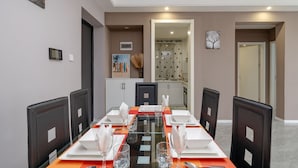 Een eetruimte met een lange tafel gedekt voor vier personen, omringd door donkere stoelen. Achtergrond toont een keuken met een modern design.