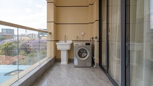 Een balkon met een wasmachine, een wastafel en een glazen deur naar uitzicht over de stad.