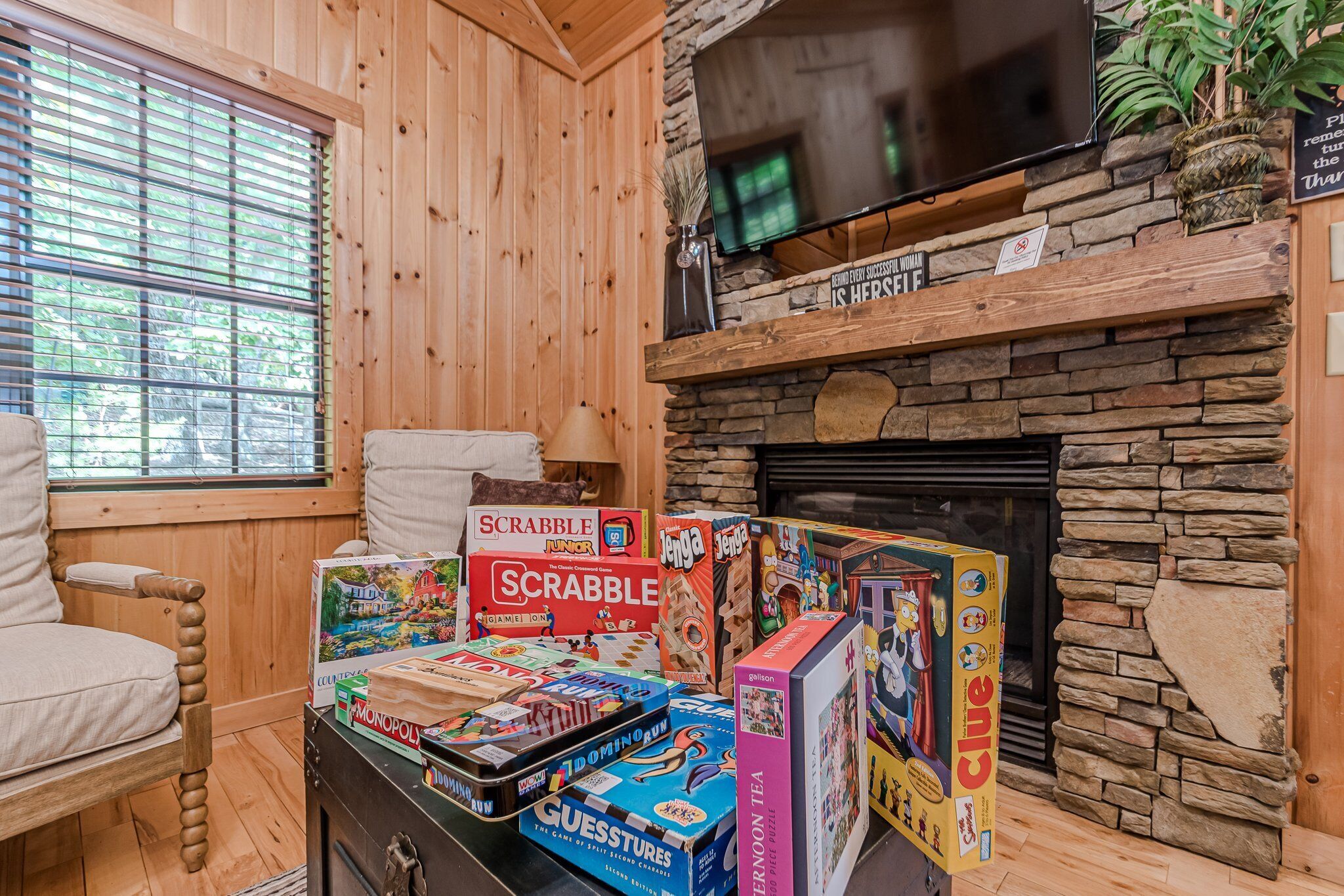 A cozy room with wooden walls, a stone fireplace, and a variety of board games on a table.