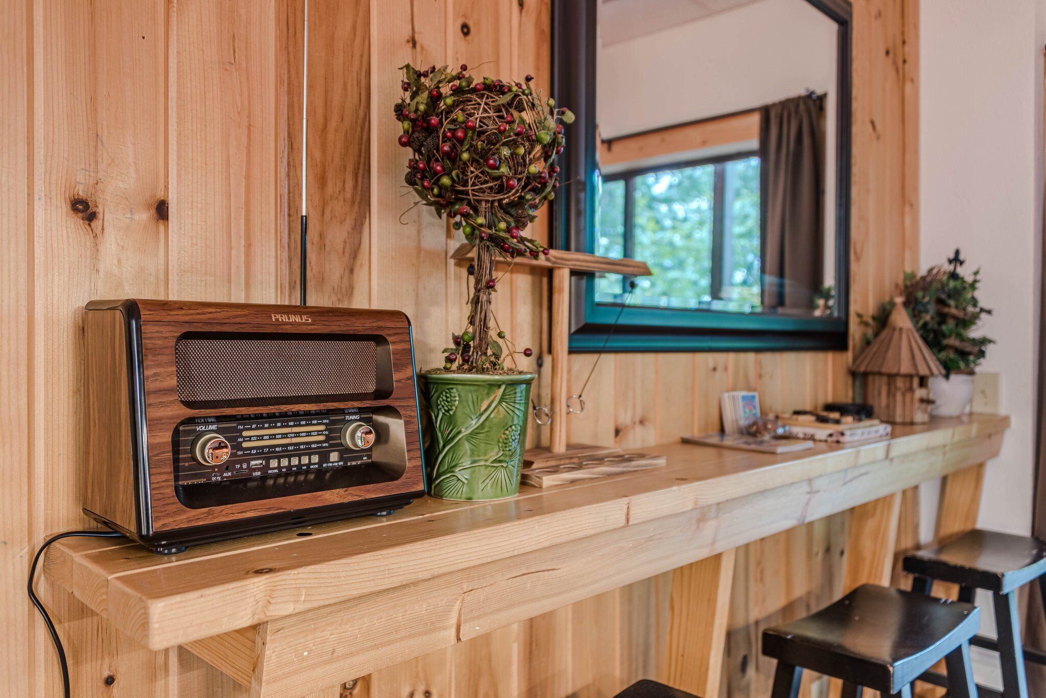 Un coin bar en bois, avec une radio ancienne, une plante en pot et une fenêtre avec des rideaux.
