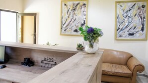 A reception area with a wooden desk, a computer, a vase with flowers, and a couch. There are two abstract paintings on the wall and a sign that reads "KEYS".