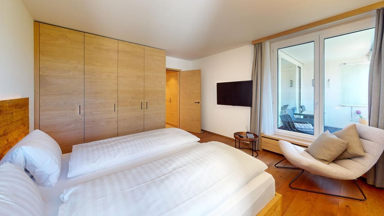 A hotel room with two beds, a wooden wardrobe, a TV, a chair, and a balcony with a view.