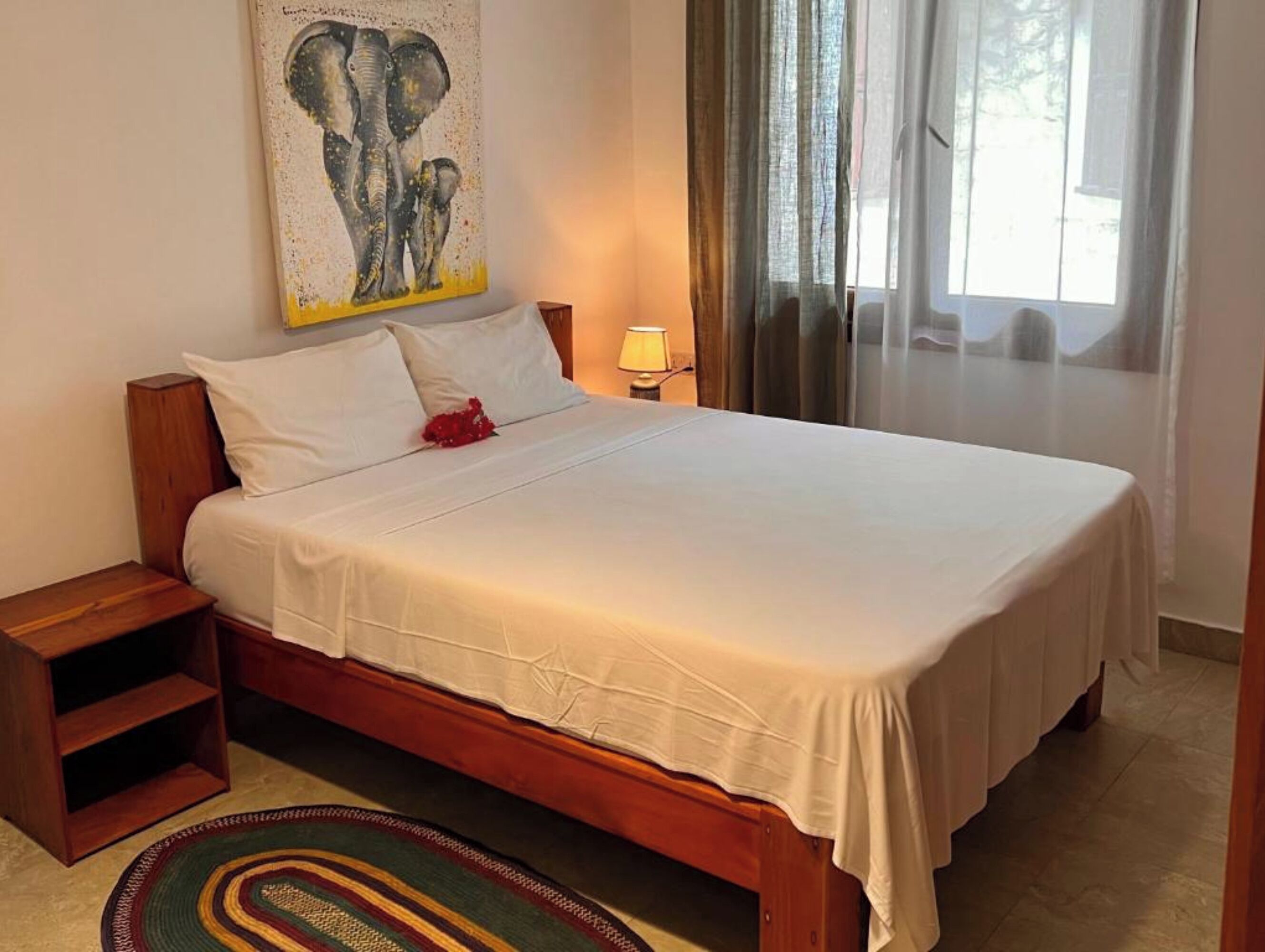 Una cama bien hecha con sábanas blancas, cabecera de madera y una alfombra colorida.