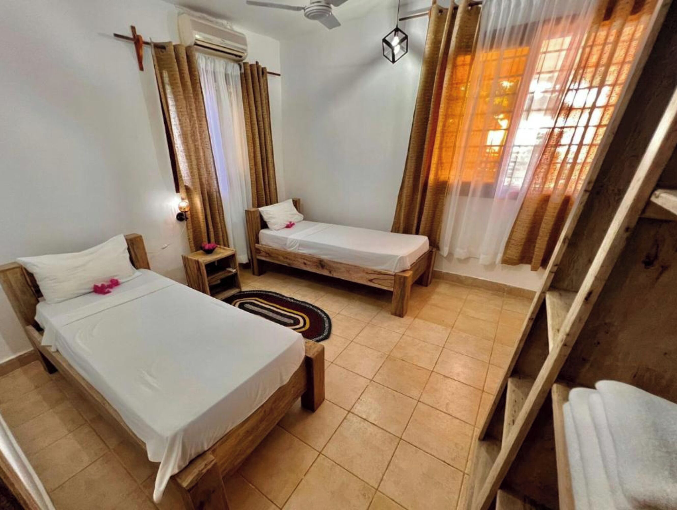 Ein Zimmer mit zwei Holzbetten, einem Deckenventilator und einem mit Vorhängen versehenen Fenster.