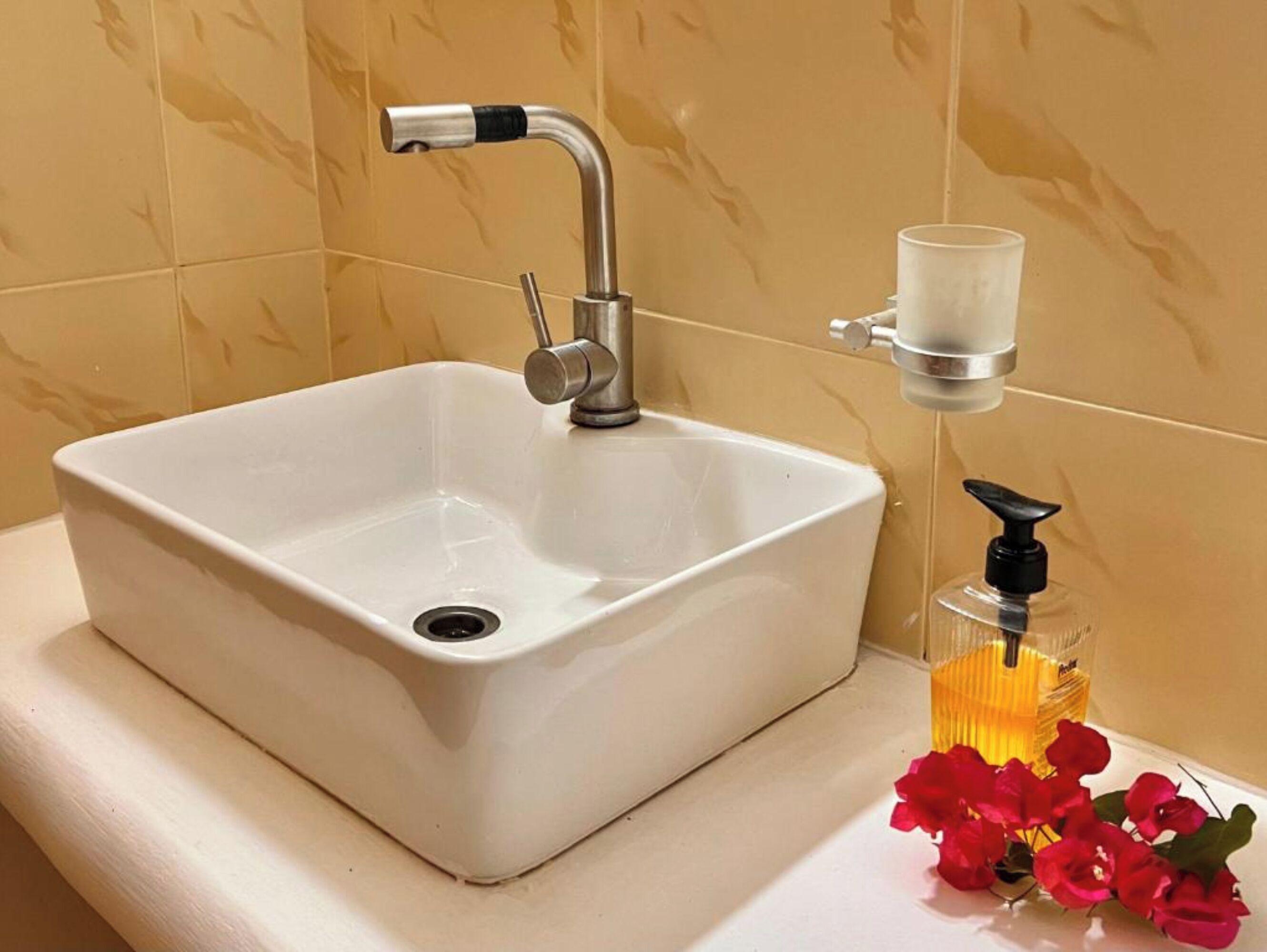 A bathroom sink with a modern faucet, a glass soap dispenser, and a glass candle holder on the countertop.