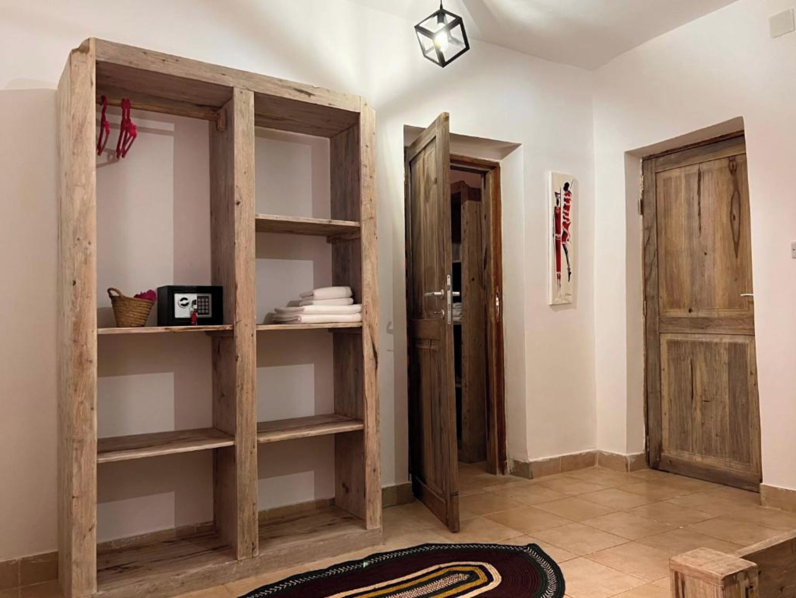 A room with a wooden wardrobe, a door, a tiled floor, and a hanging light fixture.