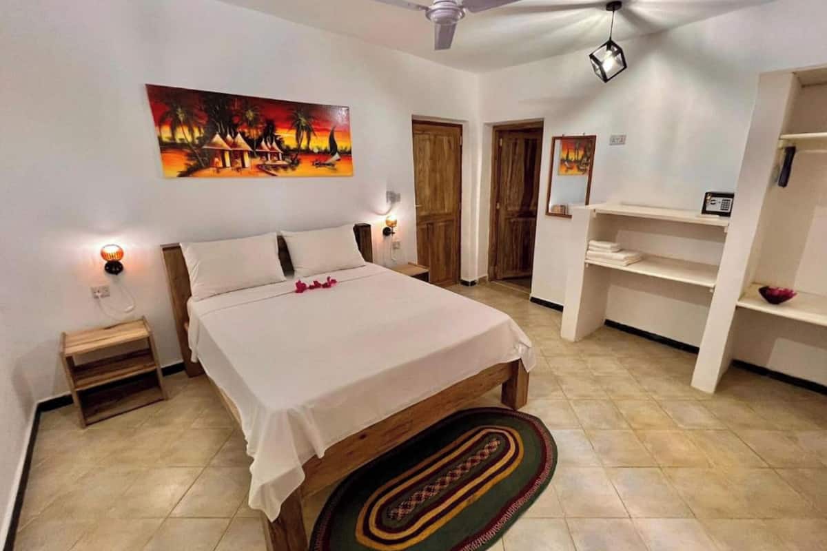 Ein Schlafzimmer mit einem Bett, Nachttischlampen, einem Gemälde, einem Deckenventilator und einem kleinen Holznachttisch.