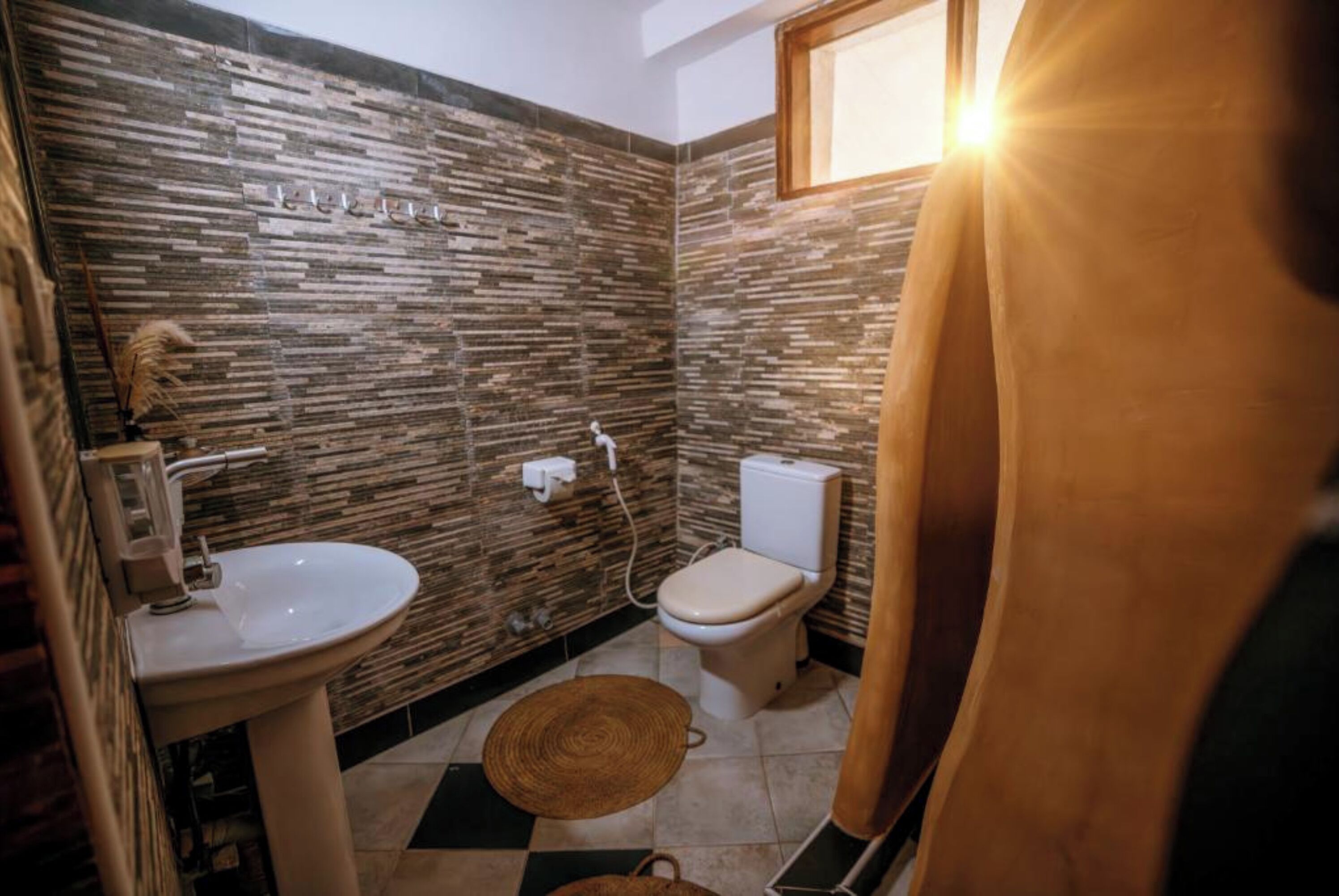 A bathroom with a stone-patterned wall, a white sink, a toilet, and a shower area.