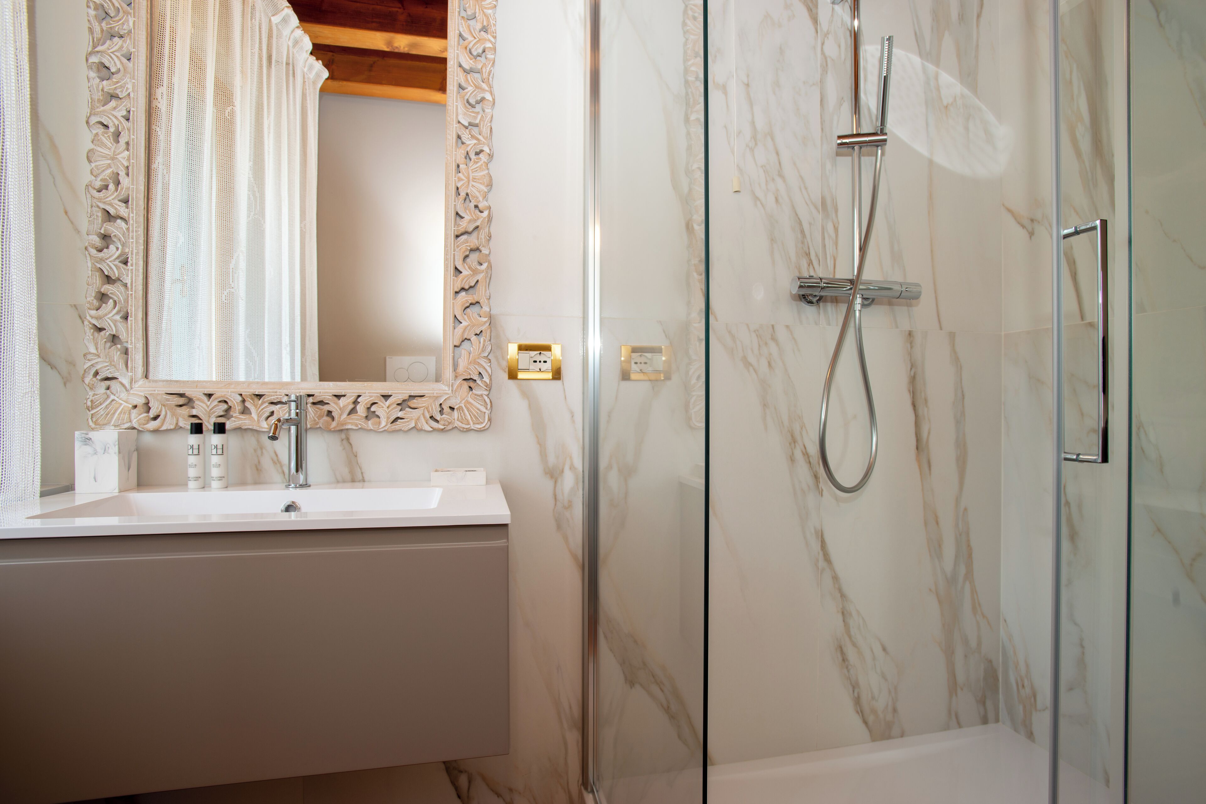 A bathroom with a marble sink, a large mirror with an ornate frame, and a glass-enclosed shower area.