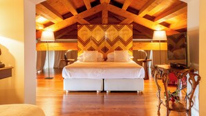 A bedroom with a large bed, two bedside tables with lamps, a television on a wooden table, and a decorative wall panel. - Tenuta Castagnera (Tarzo)