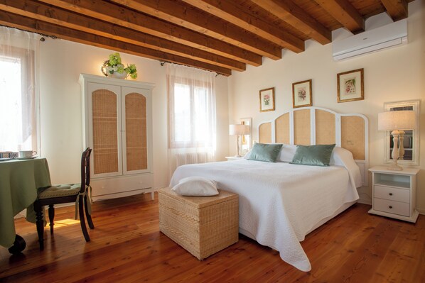 Ein Schlafzimmer mit einem großen Bett, einem Korbstuhl, einem kleinen Tisch mit grüner Tischdecke und einem weißen Schrank.