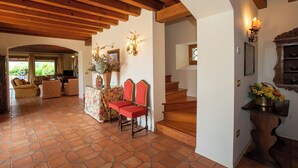 A spacious living area with a wooden staircase, a fireplace, and a dining area with a floral tablecloth. - Tenuta Castagnera (Tarzo)