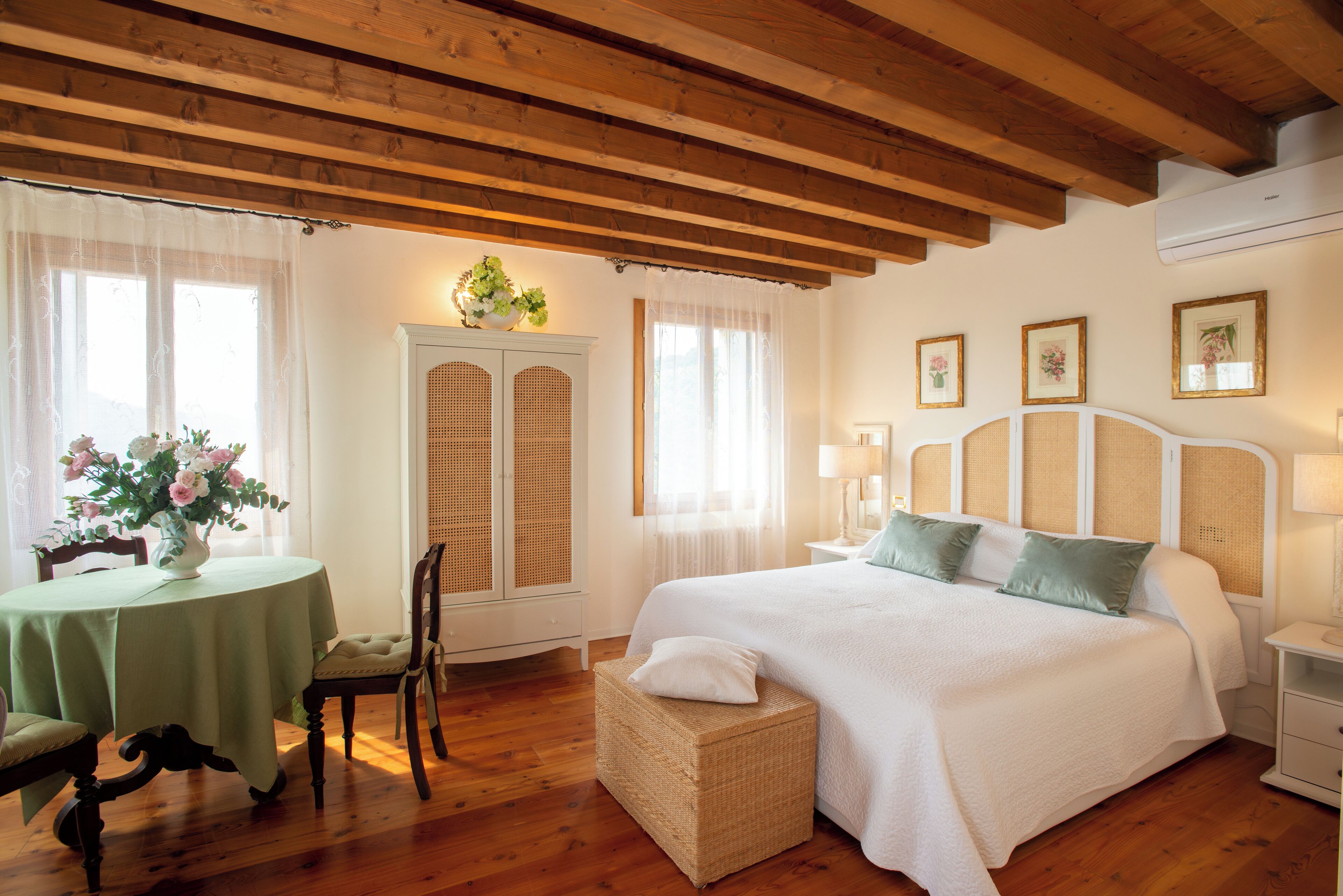 Une chambre à coucher comprenant un lit, une table de chevet, une commode, une fenêtre avec des rideaux, un plafond en bois et une table avec une chaise.