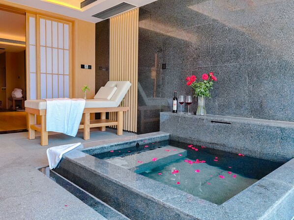 A spa room with a massage chair, a stone bathtub with rose petals, and a wooden reception desk. - Yunnan Dianchi Garden Resort & Spa (Kunming)