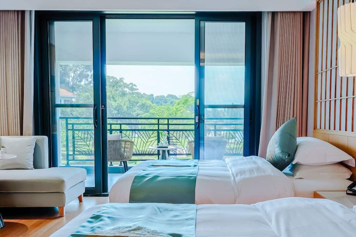 Ein Hotelzimmer mit zwei Betten, einem Sofa und einem Balkon mit Blick auf Grünflächen.