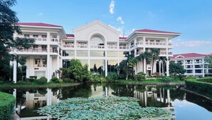 A large, multi-story building with a central courtyard, surrounded by lush greenery and a pond with lily pads.