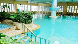 An indoor swimming pool with clear blue water, a central fountain, and steps leading into the pool.