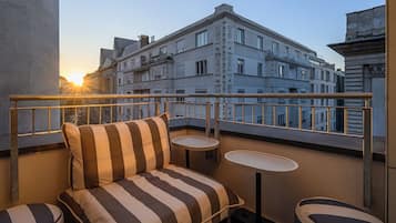 A balcony with a striped sofa, two small tables, and a view of surrounding buildings during sunset.