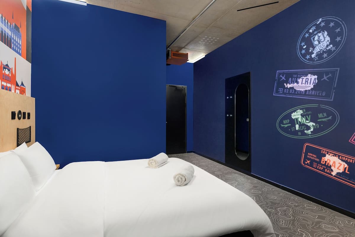 A hotel room with a large bed, a blue wall, and various travel-related stickers.