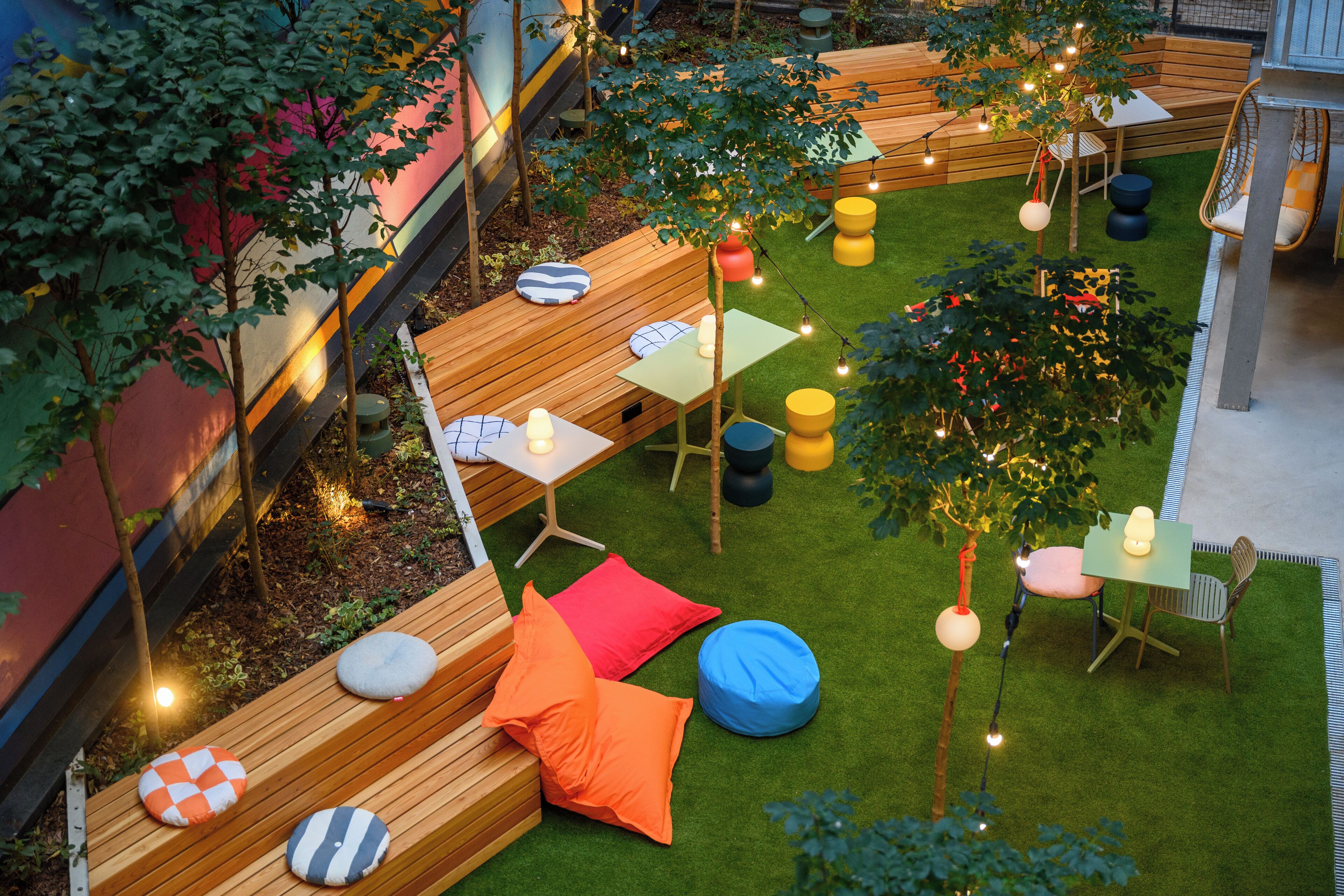 Un espace extérieur aménagé avec des bancs en bois, des coussins colorés et des guirlandes lumineuses.
