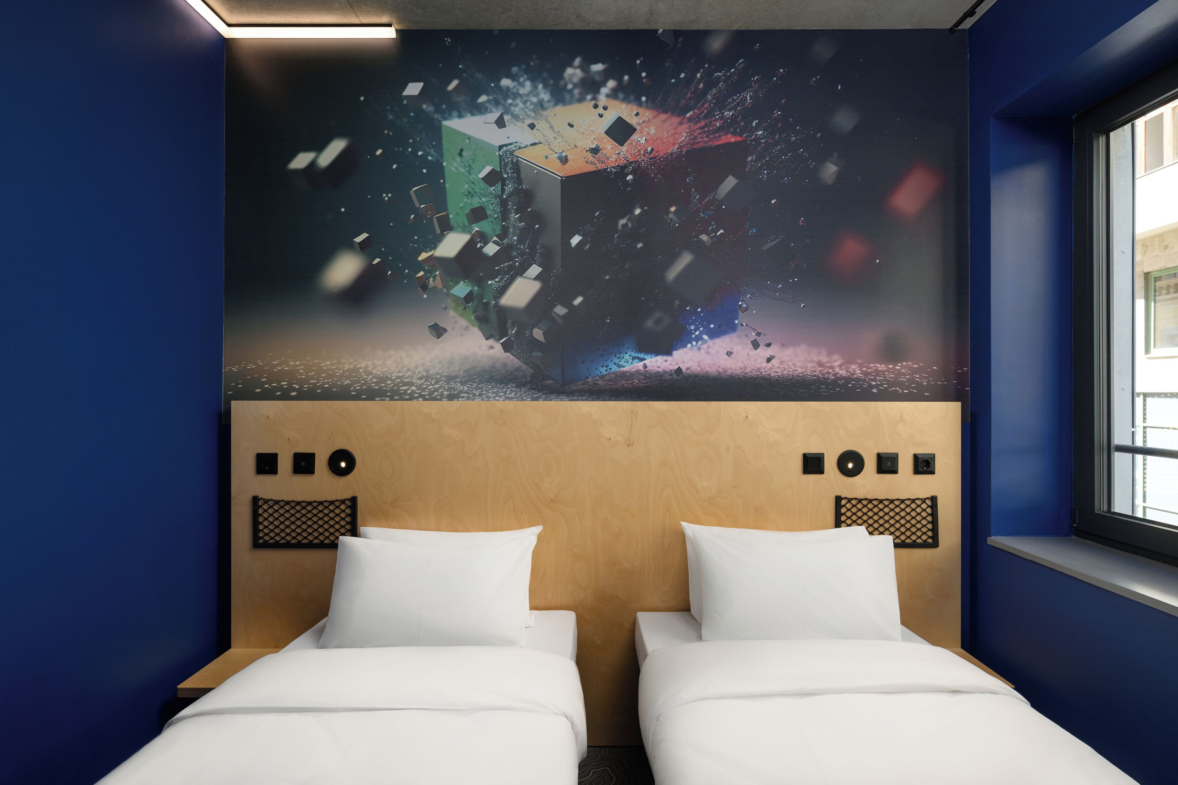 Una camera d'albergo con due letti, una testiera in legno e un'ampia opera d'arte digitale appesa al muro.