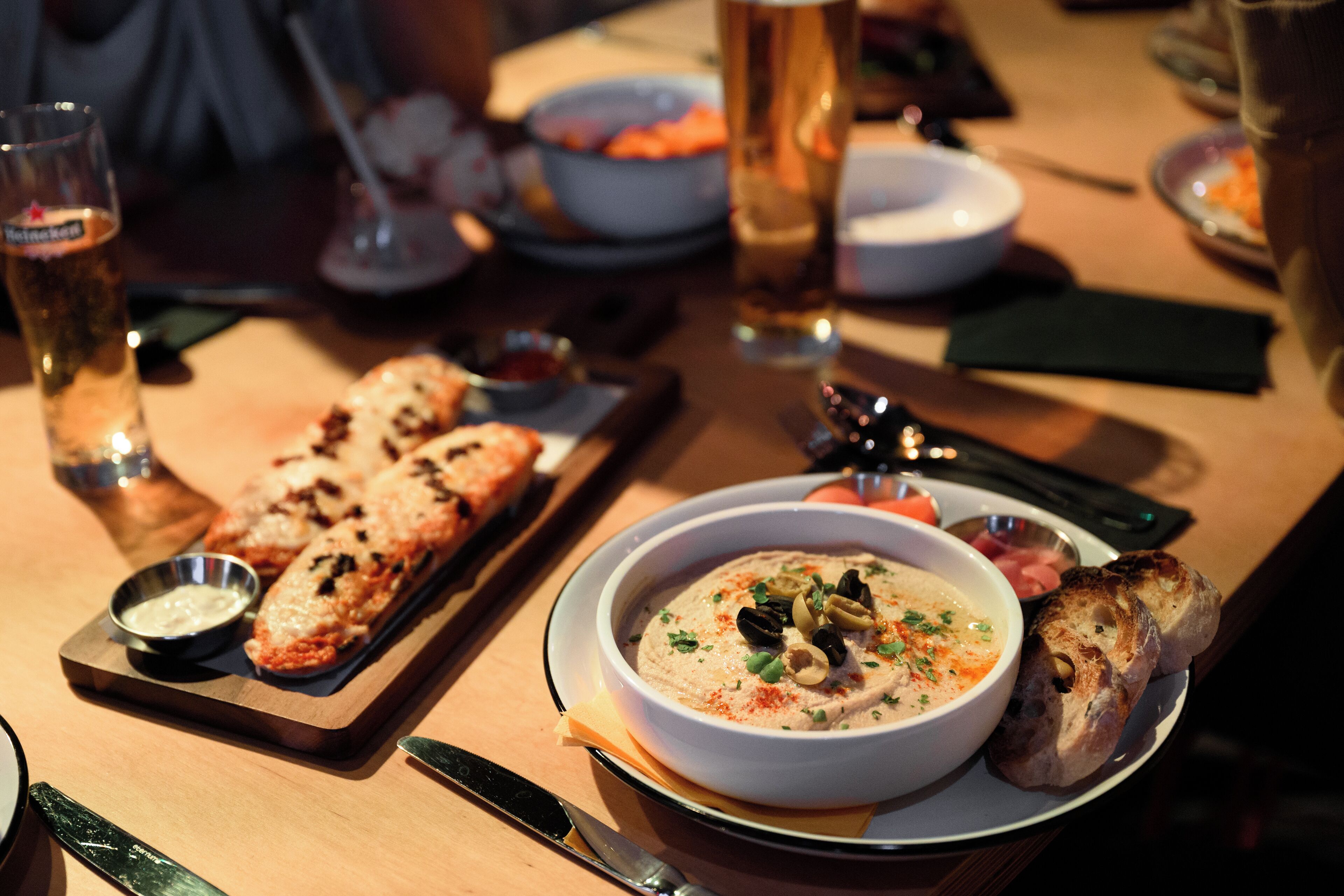 A dining table with a bowl of soup, a loaf of bread, and a glass of beer.