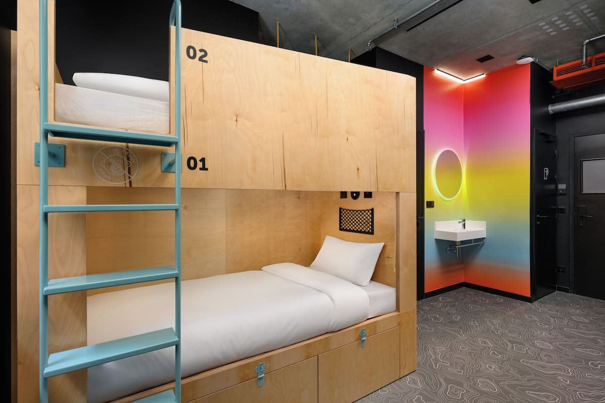 A bunk bed with a ladder, a small desk, and a wall-mounted sink.