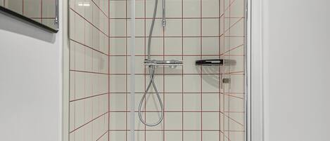 En modern dusch med en glasdörr, ett duschmunstycke som kan hållas i handen och en handhållen blandare.