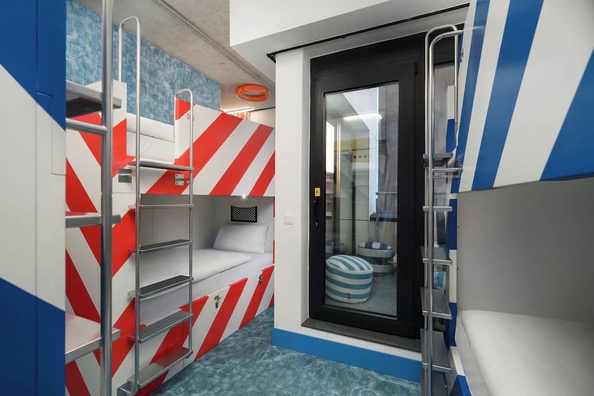 A compact, modern room with a bunk bed, a small seating area, and a glass door leading to a bathroom.