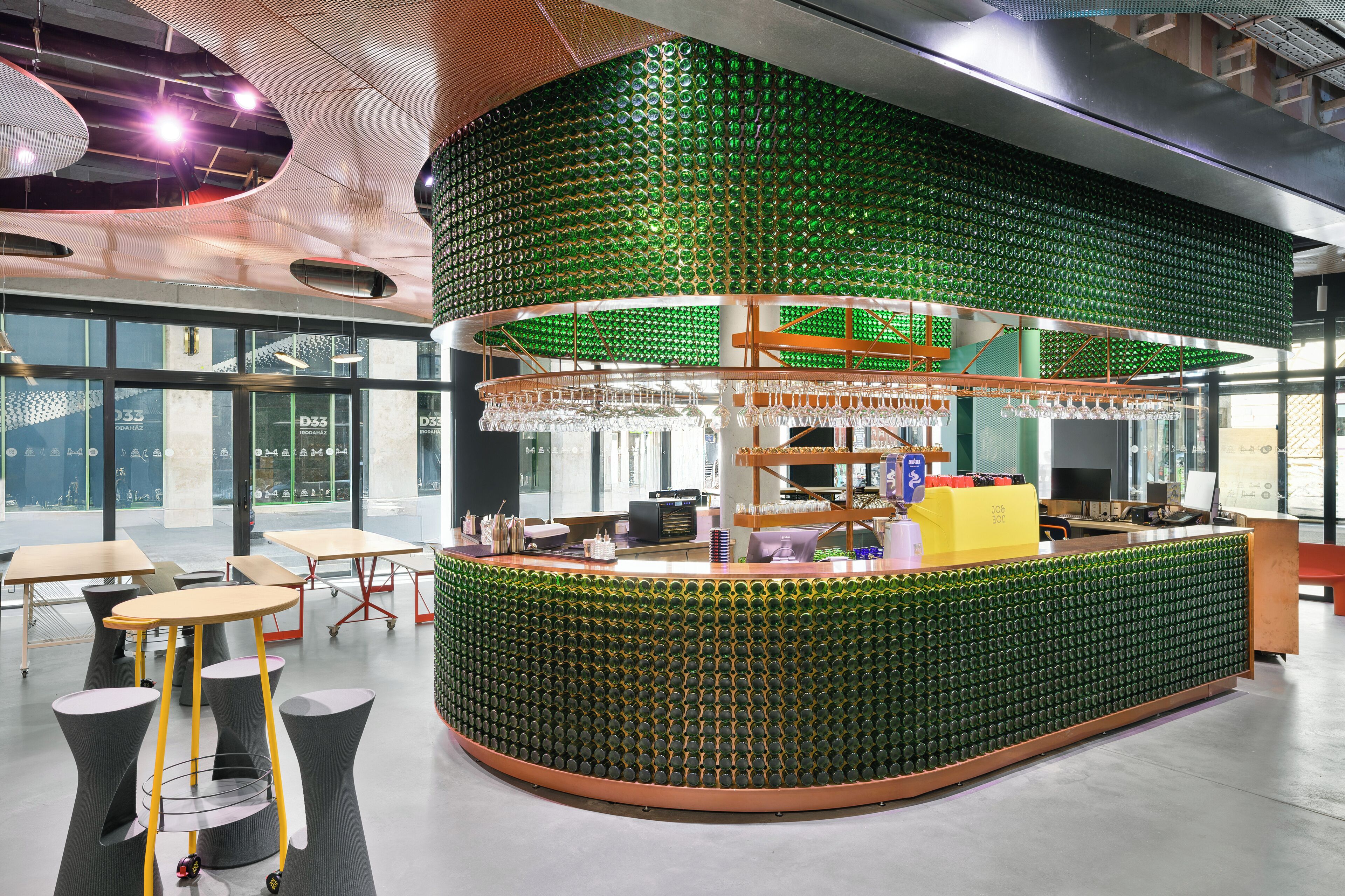 A modern bar area with a green bottle wall, seating, and a counter with a computer.
