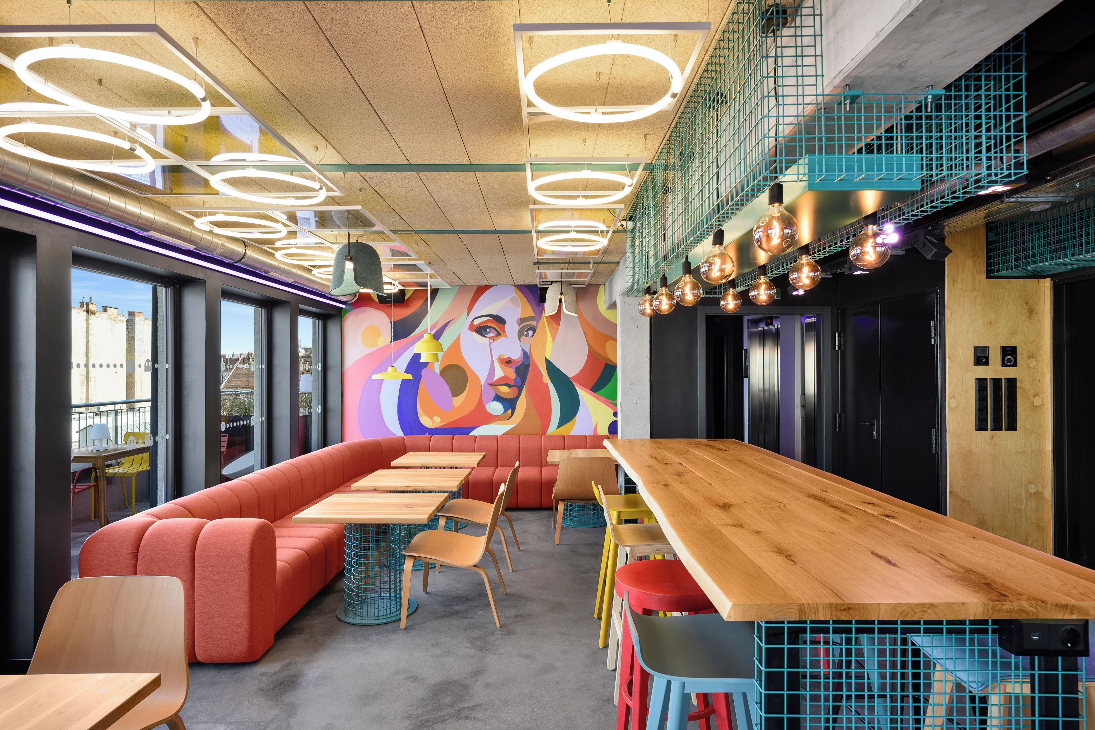 Un restaurante moderno con una larga barra de madera, asientos coloridos y un mural vibrante en la pared.