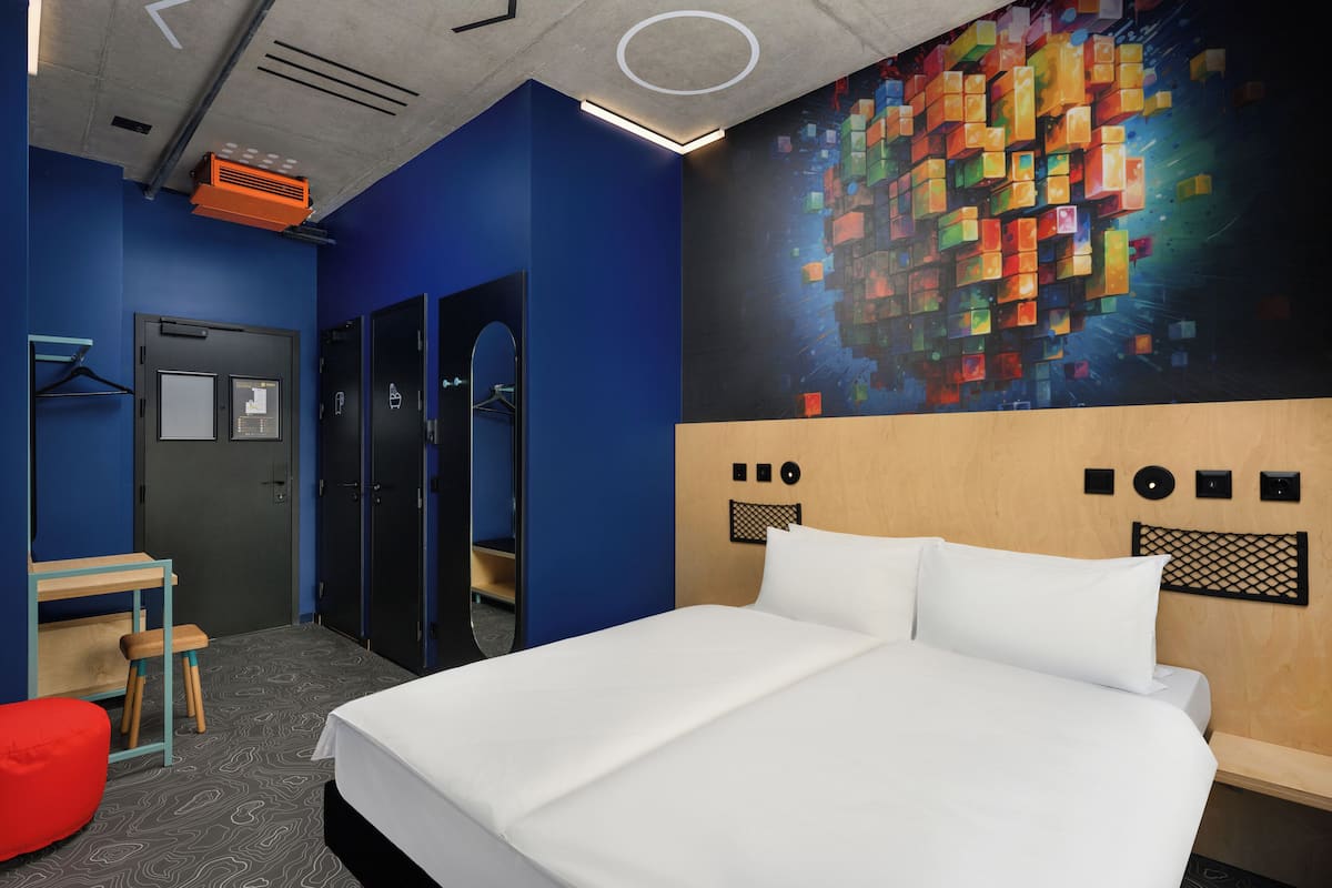 A modern hotel room with a large bed, a desk, and a wardrobe.