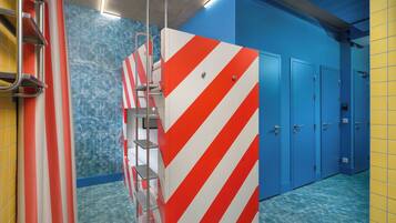 Um banheiro com piso em azulejos azuis e amarelos, parede listrada em vermelho e branco, e porta azul.