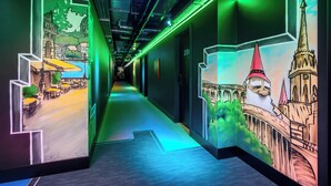 A hallway with illuminated murals depicting cityscapes and architectural landmarks. - JO&JOE Budapest (Budapest)